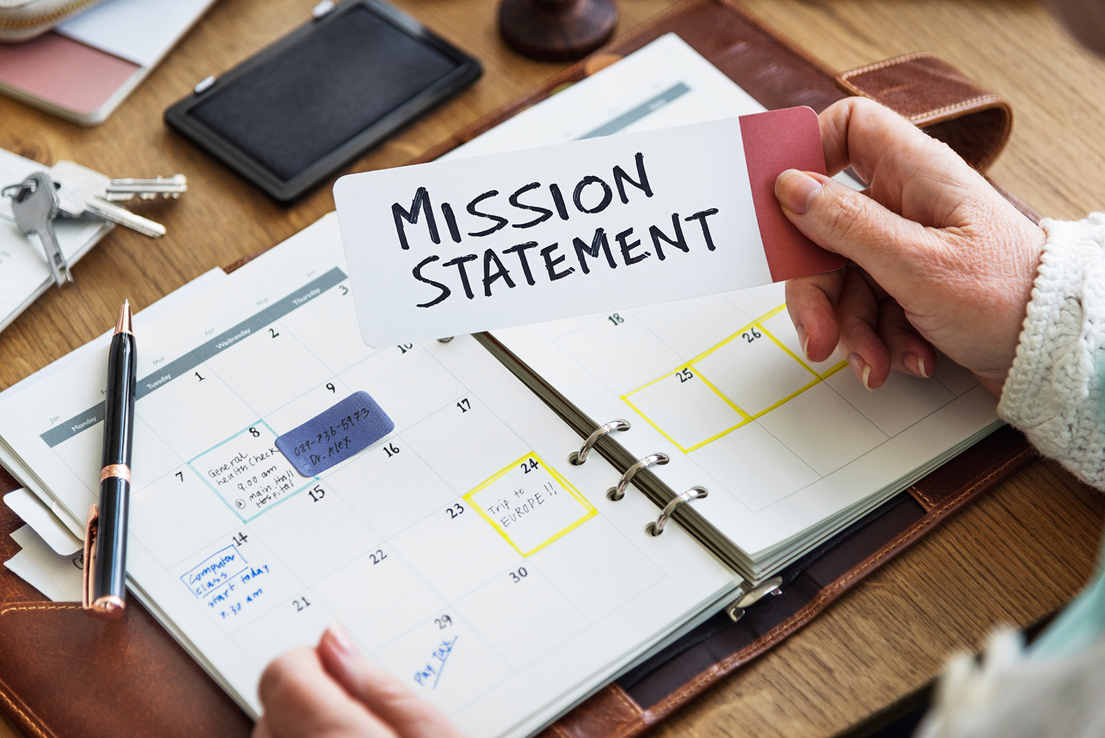 Writing a personal mission statement: a hand holding a card that reads Mission Statement over an open planner on a wooden desk