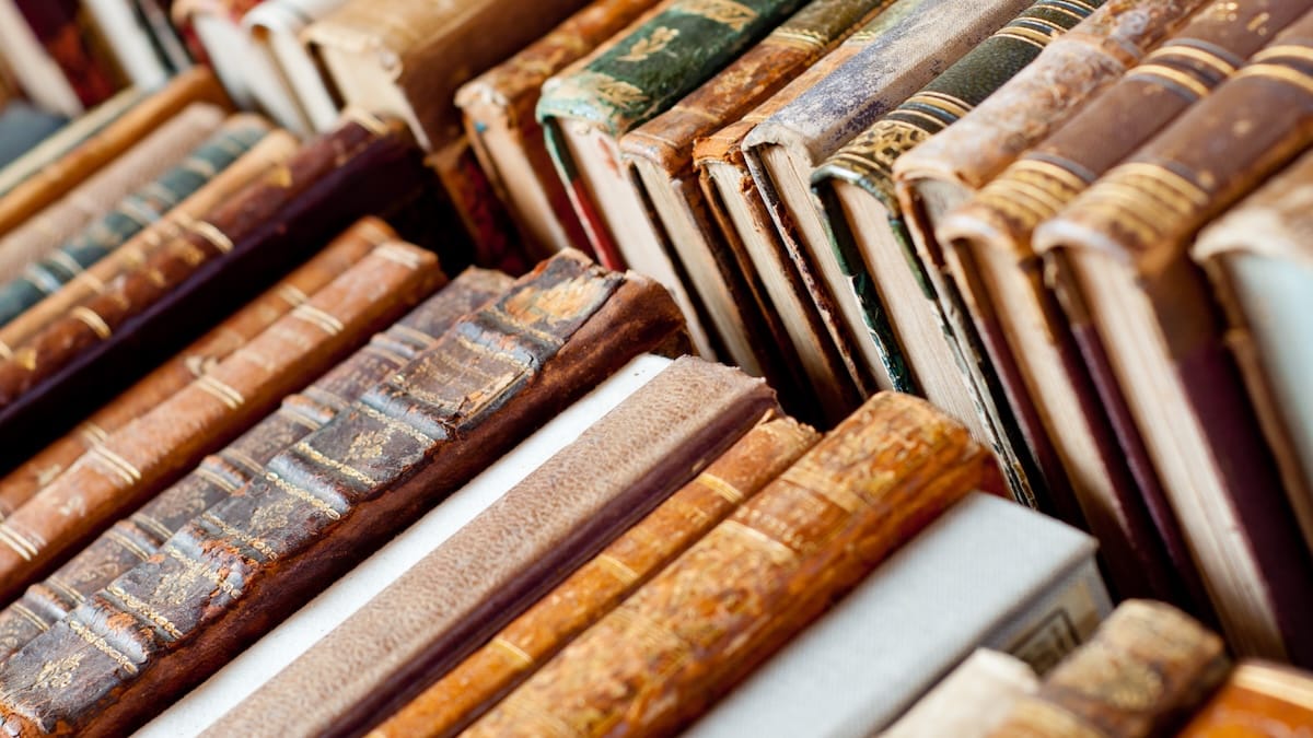 A stack of well-worn classic books on a desk in warm light