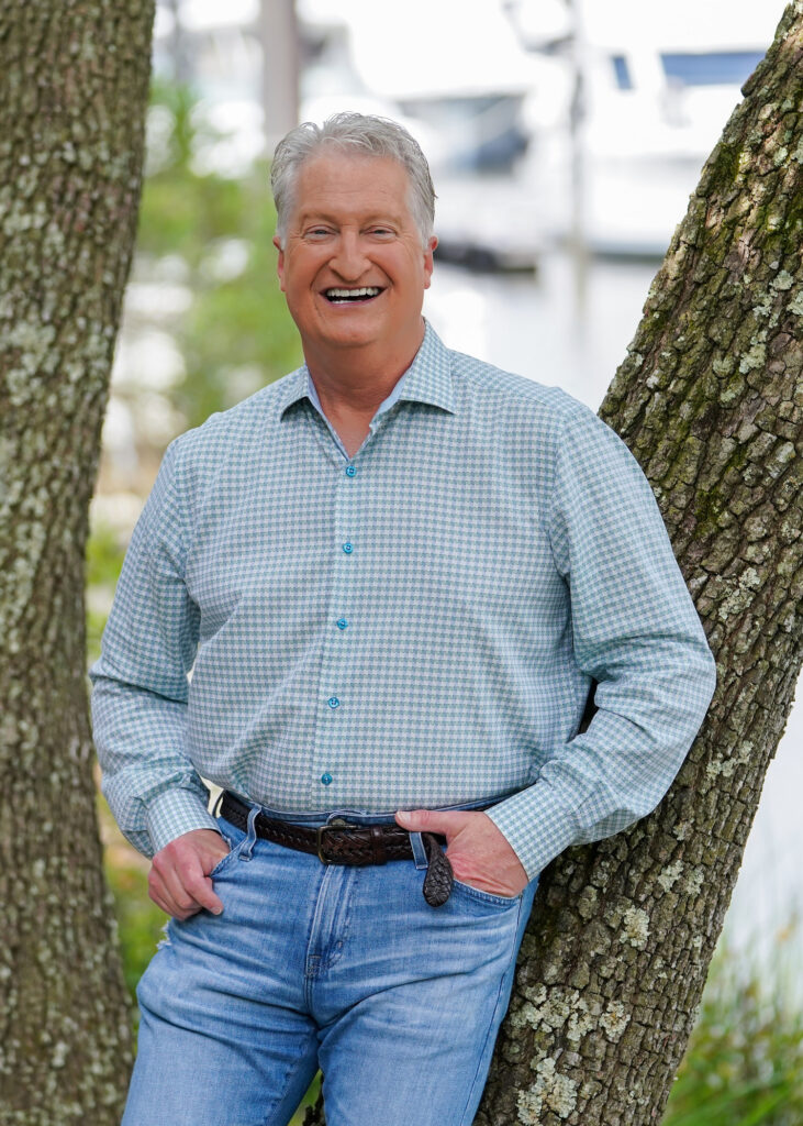 Andy leaning against an oak tree at a marina, smiling