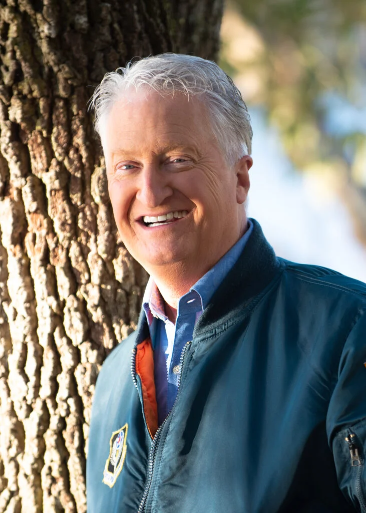 Andy Andrews smiling outdoors beside a tree