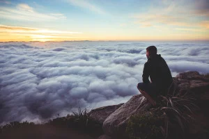 A person sitting on a rocky peak above a sea of clouds